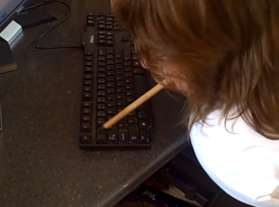 image of a woman without arms using a mouthstick to type on a keyboard